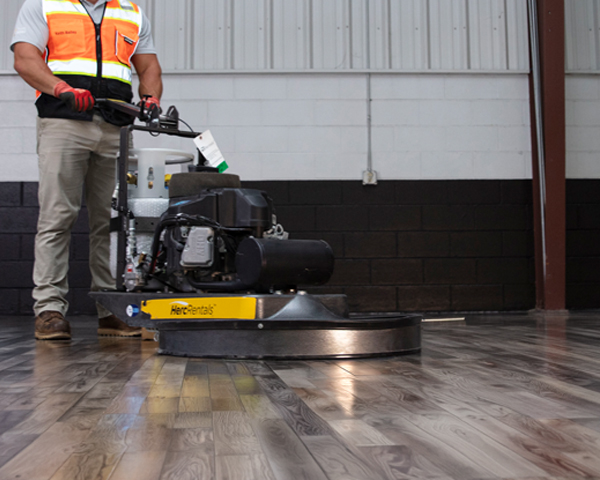 An employee operates Herc Rentals flooring restoration equipment over hardwood floors. 