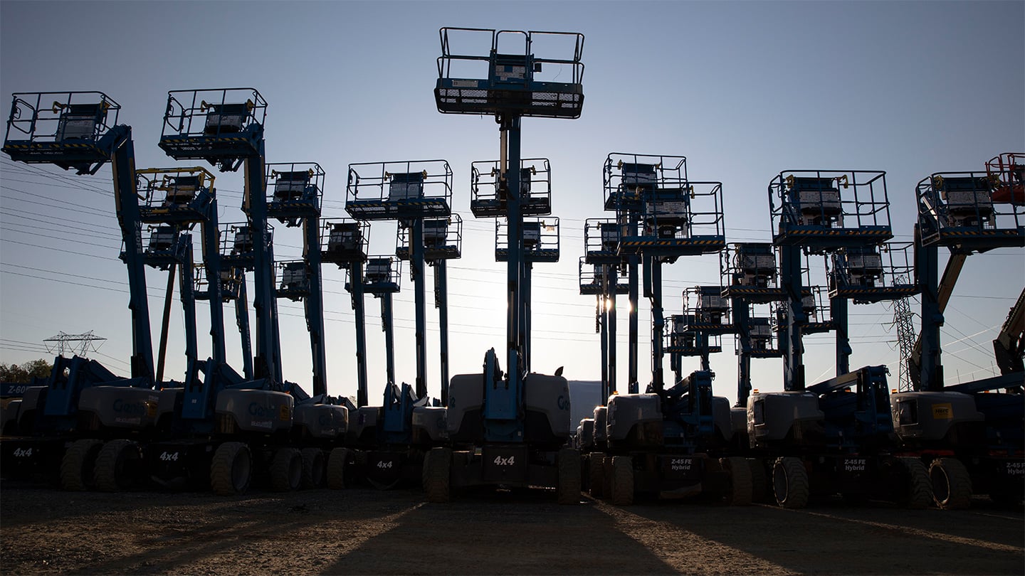 A variety of boom lifts are pictured amidst a sunset.