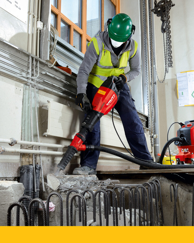 A worker wearing proper PPE demonstrates the importance of ergonomic tools as they jackhammer through concrete. 