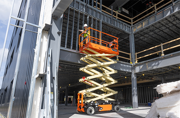 There are many types of scissor lifts and their uses vary depending on the jobsite environment and task at hand. A worker uses a scissor lift inside a facility as it's being constructed. 